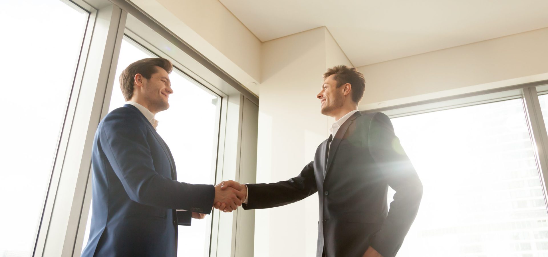 Smiling executive director handshaking with business partner in office, thanking company manager for good work, congratulating employee with promotion. Successful negotiation, strong partnership